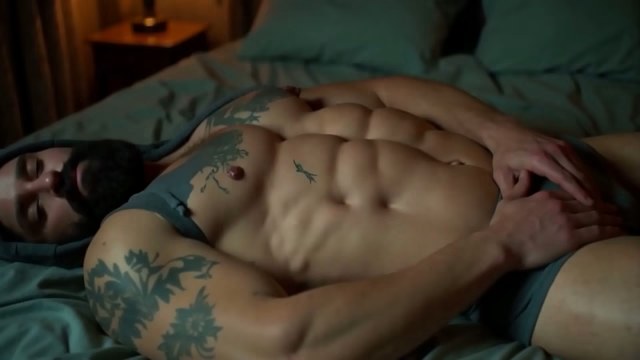Bearded muscular figure reclining on blue-green bedding in gray briefs